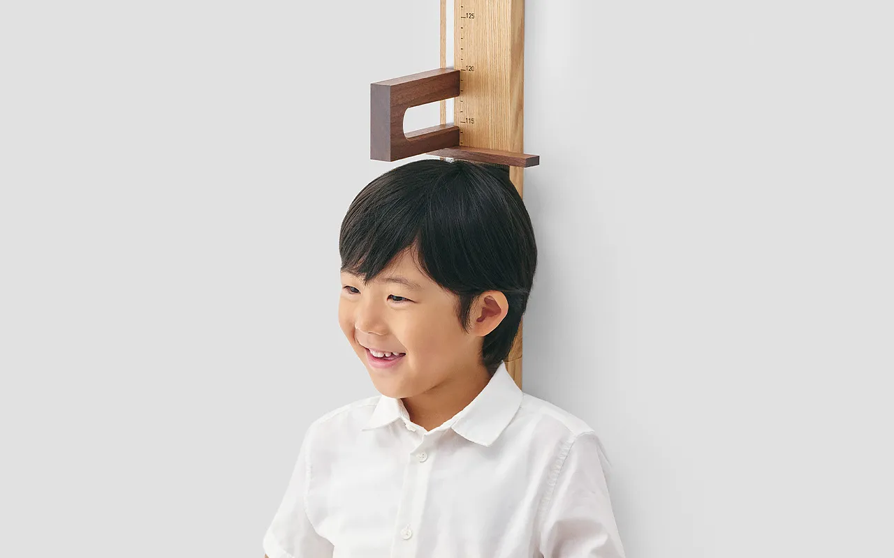 木製の身長計 スライダーを頭に合わせて身長を測る子ども